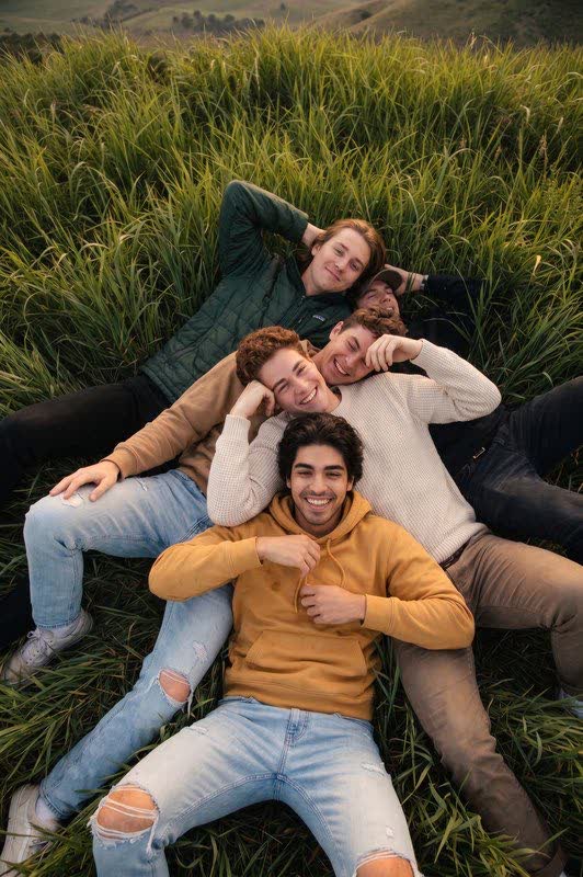 Friends lying together in a grassy field smiling